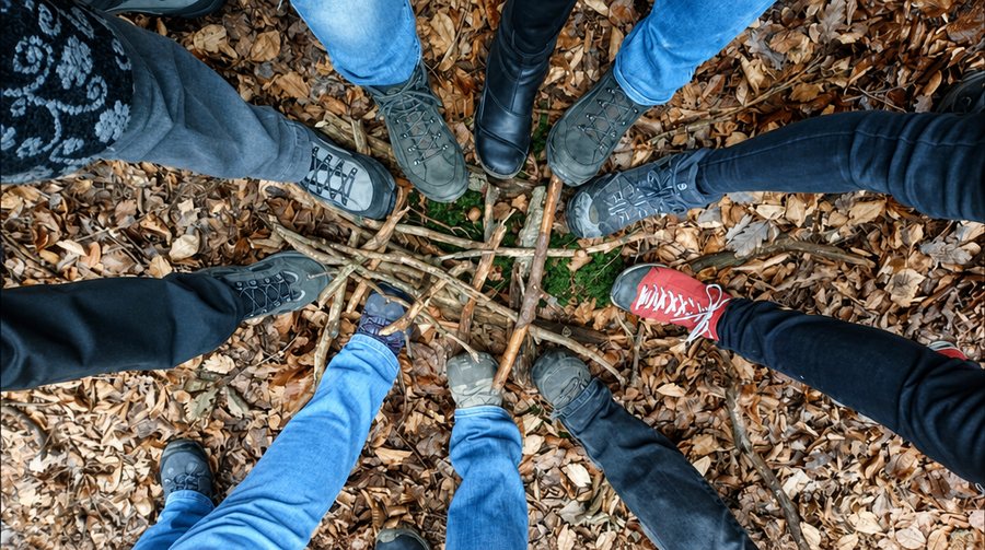Wanderschuhe im Kreis um einen Stern aus Ästen auf dem Waldboden.