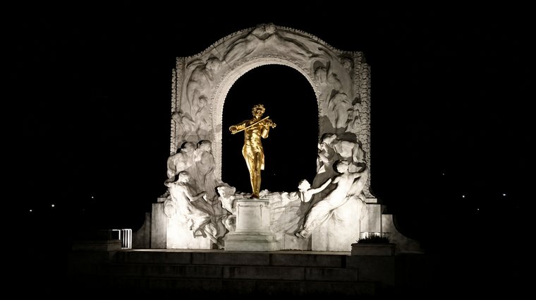 Das golden beleuchtete Johann-Strauß-Denkmal im Wiener Stadtpark am Abend.
